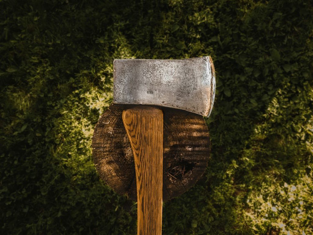 Rustic axe embedded in firewood, symbolizing preparation for Bliss Mobile Sauna’s authentic wood-burning sauna experience
